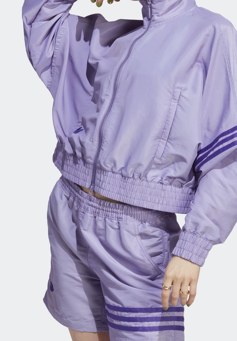 Vaaleanlila urheilusetti, johon kuuluu lyhyempi takki vetoketjulla, sivutaskuilla ja yhteensopivat shortsit, joissa on elastinen vyötärö ja raidat.