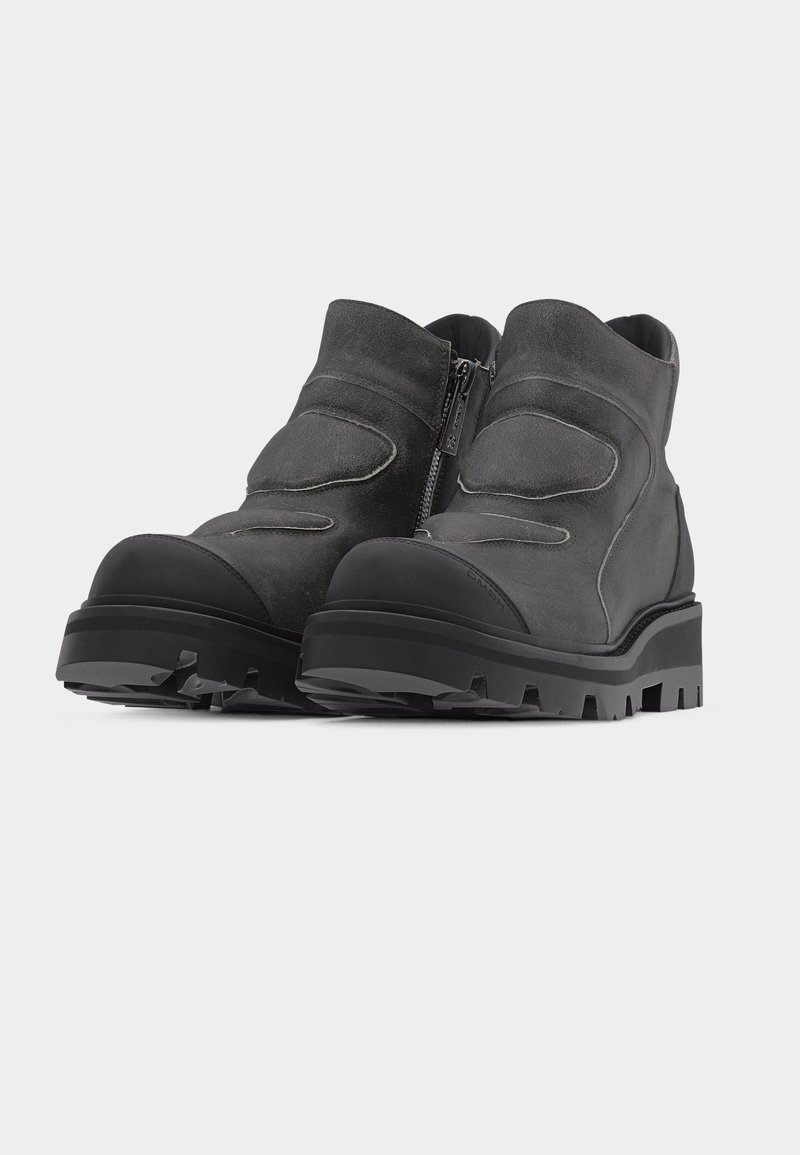 Pair of black chunky ankle boots with rugged soles and side zipper on a light background