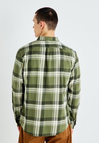 Zielona koszula flanelowa w kratę z białymi i czarnymi wzorami, z długimi rękawami i standardowym kołnierzykiem. Miękka tekstura i swobodny styl.