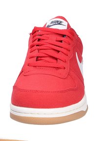 Zapatilla de lona roja con logotipo y acentos blancos. Presenta puntera redonda, superficie texturizada y suela de goma. Cierre con cordones y cordones planos.