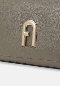 Gros plan sur un cuir texturé taupe avec un emblème métallique doré en forme de lettre U inversée avec une barre horizontale.