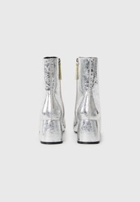 Silberne Knöchelstiefel mit metallic Finish, glatter Textur, seitlichen Reißverschlüssen und Blockabsätzen. Verfügt über leichtes Rissmuster.