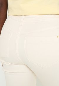 Jeans de mezclilla beige claro con un diseño ajustado, que presentan bolsillos traseros y costuras decorativas, textura suave y una cintura de altura media.