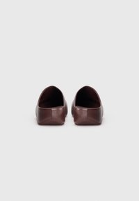 Ballerines en cuir marron avec une texture lisse, un bout rond et un design minimaliste. Les talons sont bas et légèrement texturés pour une meilleure adhérence.