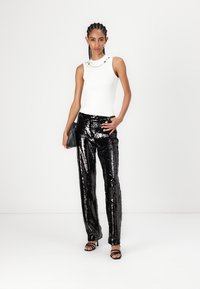 Haut sans manches blanc avec un col rond, associé à un pantalon à paillettes noir taille haute qui scintille. Le mannequin tient un sac à main noir et porte des talons fins.