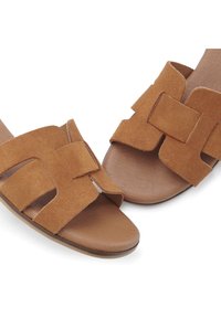 Brown suede sandals featuring wide straps with a cut-out design, soft flat soles, and a smooth, tan inner lining.