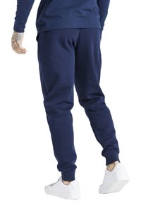 Námořnické modré tepláky z měkkého materiálu, se širokým elastickým pasem a manžetami na kotnících, v kombinaci s bílými teniskami pro kontrast.