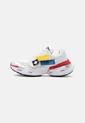 Zapatilla blanca con suela negra, parches de tela multicolor, detalles en rojo y texto escrito a mano en la suela y los costados.