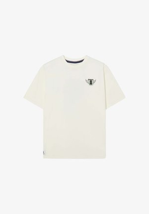 Camiseta de manga corta color crema, hecha de algodón, con un pequeño logo verde y negro con alas en el pecho izquierdo. Diseño de cuello redondo.