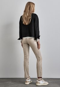 Zwarte suède jas met een losse fit, beige leren broek en witte sneakers met beige accenten. Vederlichte textuur en eenvoudig ontwerp.