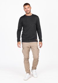 Camiseta negra de cuello redondo y manga larga con costuras visibles, combinada con pantalones cargo beige que cuentan con múltiples bolsillos, usados con zapatillas blancas.