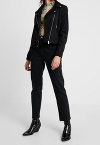 Černá semišová biker bunda se stříbrným zipem, zkombinovaná s černými džínami a lesklými kotníkovými botami, s hadím vzorem na topu pod ní.