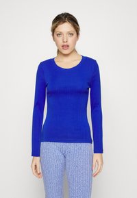 Gerippter Langarm-Top in leuchtendem Blau mit rundem Ausschnitt und figurbetonter Passform, kombiniert mit strukturierten hellblauen Hosen.