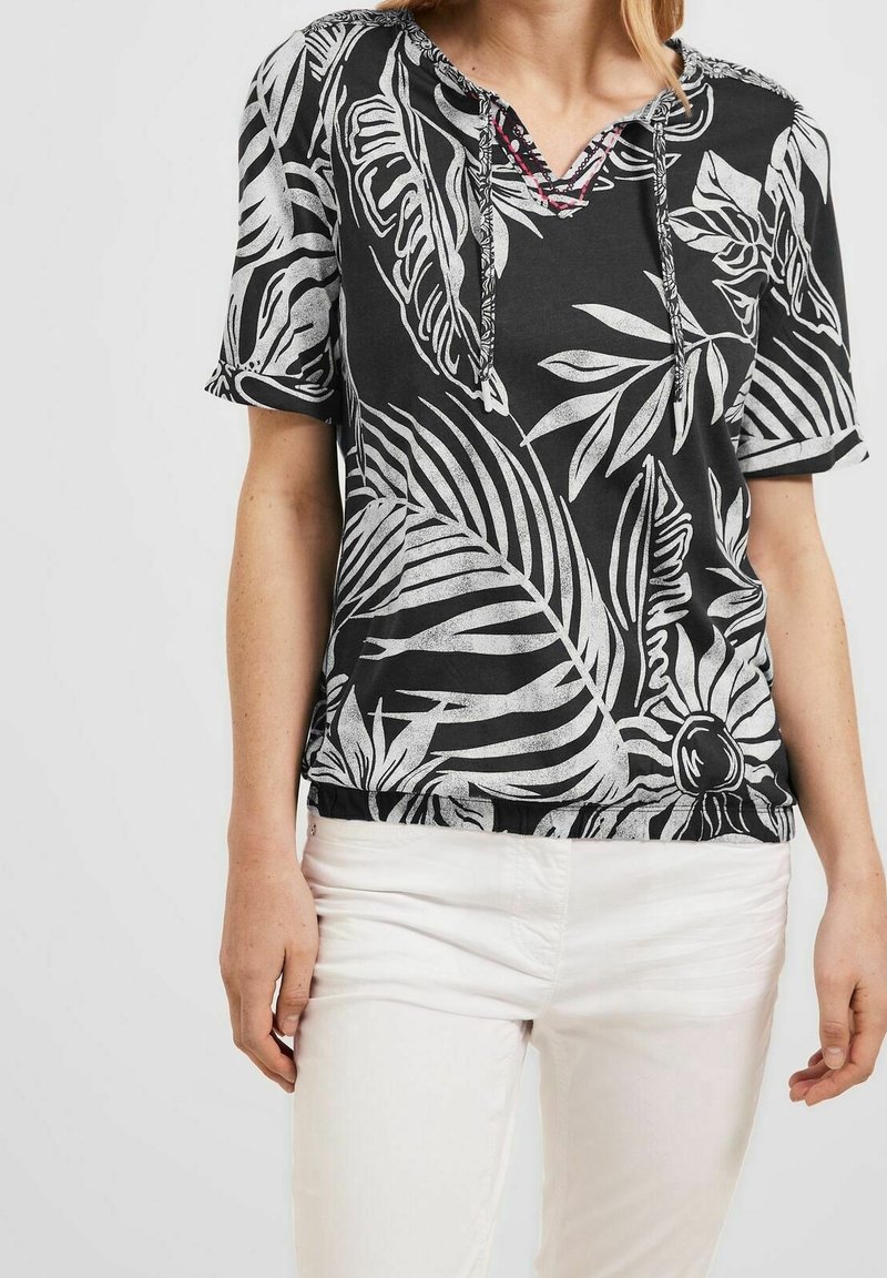 Haut noir à manches courtes avec motifs de feuilles tropicales blanches, encolure en V avec cordons de serrage et coupe décontractée à la taille.