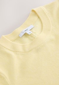 Pull jaune pâle à col rond avec col côtelé et étiquette de marque blanche visible "NEXT" cousue à l'intérieur de l'encolure.