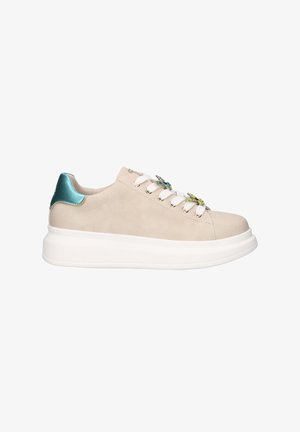 Zapatilla beige de caña baja con suela blanca gruesa, lengüeta en el talón en color verde azulado, cordones blancos y adornos decorativos con joyas a lo largo de los cordones.