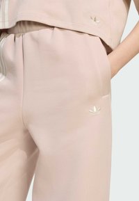 Svetlo ružové jogger nohavice s elastickým pásom, bočnými vreckami a jemne vyšitým logom. Mäkkučká tkanina s hladkou textúrou.