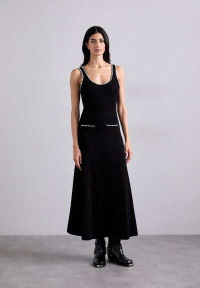 Black ribbed knit dress with sleeveless design, scoop neckline, and pearl accents on straps and pockets. Worn with black ankle boots.