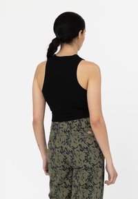 Haut sans manches noir au design ajusté, associé à un pantalon en imprimé camouflage vert avec des poches et des motifs sombres contrastants.