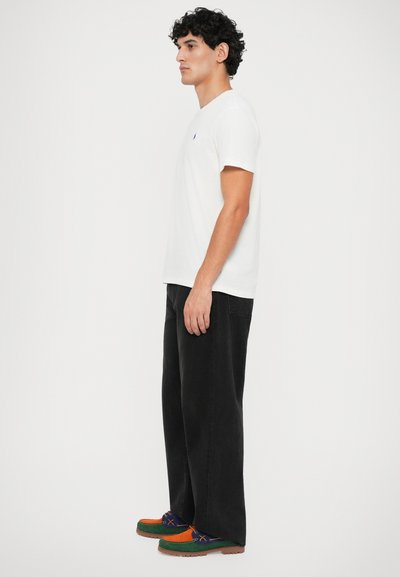 Camiseta branca de gola redonda, jeans pretos de corte largo e sapatos multicoloridos com detalhes em verde, laranja e azul. Design simples, aparência casual.
