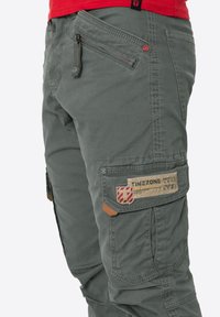 Cargo-Hosen aus olivgrünem Stoff verfügen über mehrere Taschen, ein strukturiertes Patch mit "TIMEZONE"-Markierung und aufwendige Nähte.