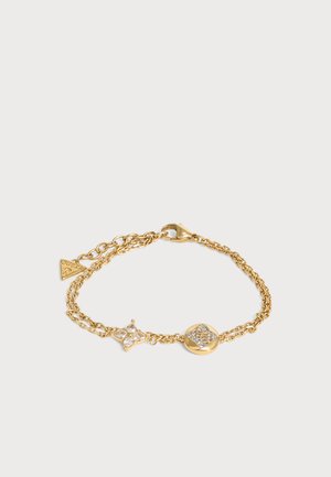 Bracelet délicat en chaîne d'or avec deux breloques décoratives ornées de pierres précieuses et un fermoir à homard sur un fond clair.