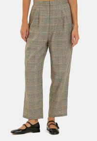 Pantalons à carreaux dans des tons doux avec une taille haute, un devant plissé et une coupe large, associés à des chaussures Mary Jane en vernis noir.