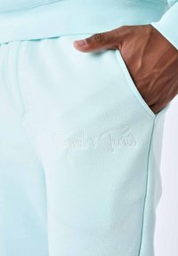 Pantalones de chándal azul claro que cuentan con una tela suave, cinturilla acanalada y un logotipo bordado de "Project x Paris" en la zona del bolsillo frontal.