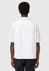 Camisa blanca de manga corta con cuello clásico, costura trasera recta y un corte holgado. La tela parece suave y ligera.