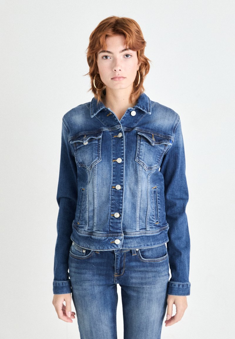 Veste en denim de différentes nuances de bleu avec un col classique, une fermeture à boutons et des poches devant. Texture lisse et coupe structurée.