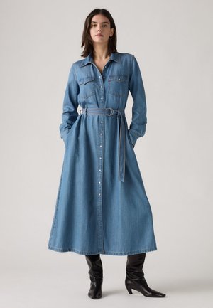 Vestido largo de camisa de mezclilla con botonadura frontal, bolsillos en el pecho y cinturón del mismo tejido; cuenta con mangas largas y una silueta fluida en A.