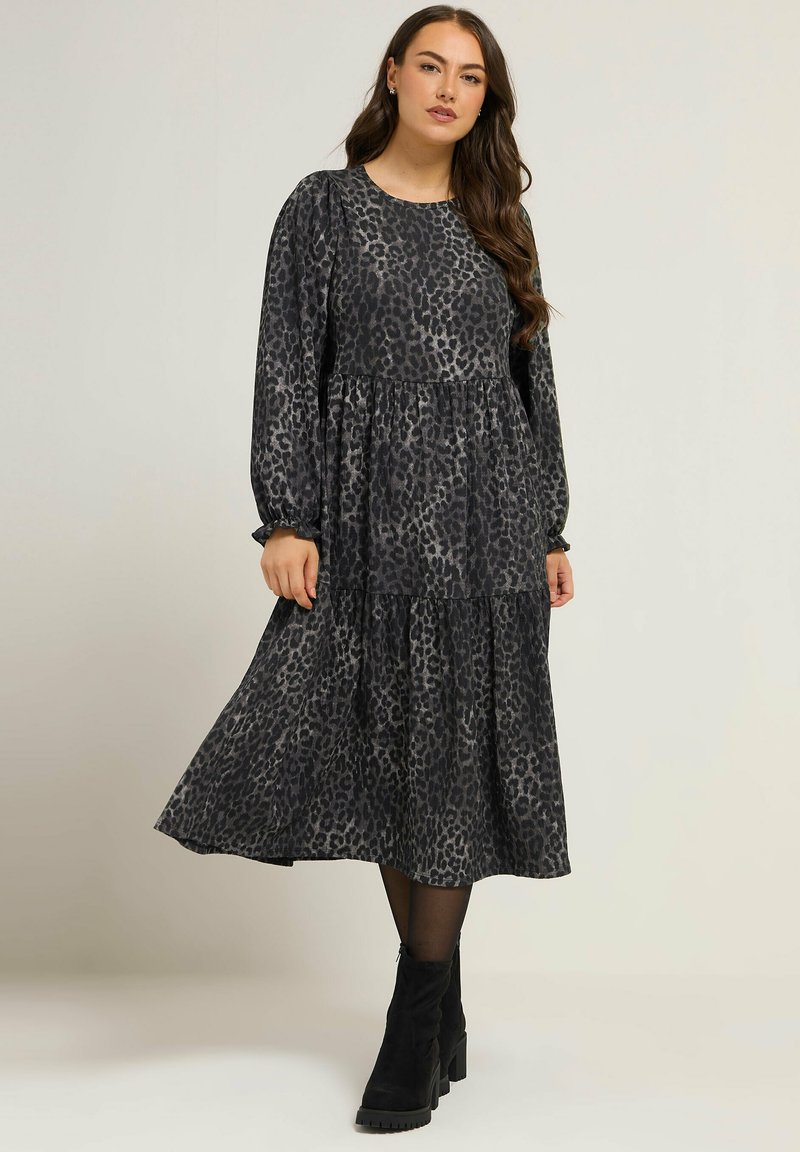 Sukienka z długim rękawem w czarny wzór panterki z warstwową, zwiewną spódnicą. Posiada okrągły dekolt i elastyczne mankiety. Połączona z czarnymi botkami za kostkę.