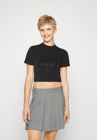 Must mustaga t-särk lühikeste varrukatega, millel on tekstuurne graafikadisain ja vale kaelus, koos kaherealise halli ruudulise seeliku ning voldikutega.