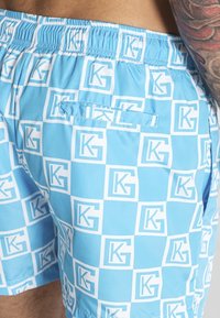 Kupanje kratke hlače svijetlo plave boje s bijelim kvadratnim uzorkom koji sadrži "KG" logo. Elastičan pojas i stražnji džep s preklopom.