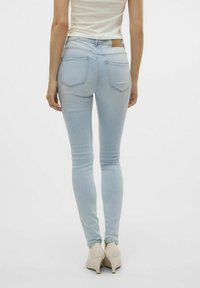 Jeans ajustados de color azul claro con dos bolsillos traseros, una etiqueta de cuero color marrón claro en la cintura y una textura suave, combinados con tacones de color claro.