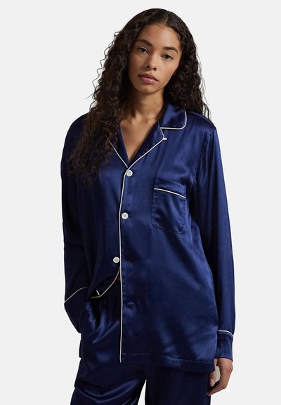 Marineblauw satijnen pyjamapak met een overhemd met knopen, witte biezen en een borstzak, gecombineerd met bijpassende broek. Glad textuur is duidelijk zichtbaar.