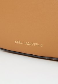 Tan leather material with a smooth texture, featuring gold embossed "KARL LAGERFELD" logo and black edging for contrast.