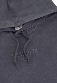 Sudadera con capucha gris de textura suave, que presenta un logo bordado y detalles con cordón. Diseño casual con un ajuste holgado.