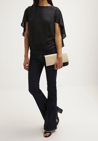 Sort, gennemsigtig top med flæseærmer, parret med mørke flared jeans og en taskeskaft i to nuancer. Sorte hæle fuldender looket.