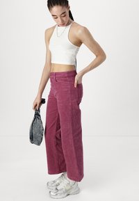 Wijde corduroy broek in donkerroze, met steekzakken aan de voorkant, een knoopsluiting en een gestructureerd ribbelontwerp, gecombineerd met een witte cropped top.