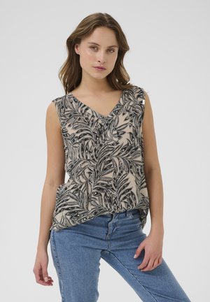 Haut sans manches beige avec un motif de feuilles noires, décolleté en V, coupe décontractée et fentes latérales discrètes. Associé à un jean en denim bleu.