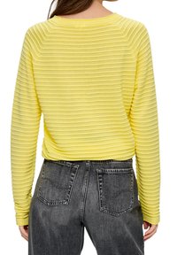 Gul, ribbad långärmad topp med vid halsringning; parat med högmidjade mörkgrå jeans i denim med bakfickor.