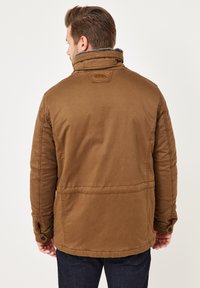 Brown padded jacket with a high collar and soft lining, featuring stitched detailing and buttoned cuffs. Textured fabric with a matte finish.