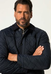 Prošívaná námořnická bunda s kordurovým límcem, vybavená knoflíkovým zapínáním a diagonálním šitím. Model má zkřížené paže.