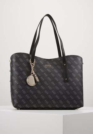 Sort Guess tote taske med mønstret logo print, dobbelte skulderstropper og guldfarvede nøglering charmetro, der hænger foran.