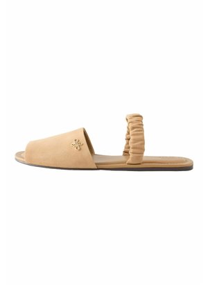 Beige platte sandaal met open teen, geplooide enkelband en klein goudkleurig decoratief embleem aan de zijkant van het voorste bandje.