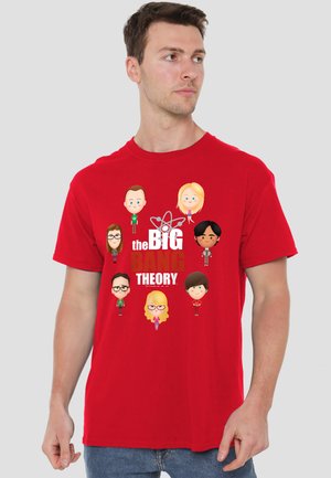 Man wearing a red T-shirt with cartoon characters and white text reading "the Big Bang Theory" on a plain gray background.