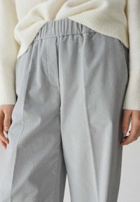 Pantaloni in corduroy grigio chiaro con vita elastica, caratterizzati da una texture a coste verticali e tasche laterali. Abbinati a un maglione color crema.