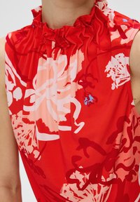 Rode mouwloze blouse met ruches bij de hals, voorzien van gedurfde bloemmotieven in tinten roze en blauw, gemaakt van een zachte stof.