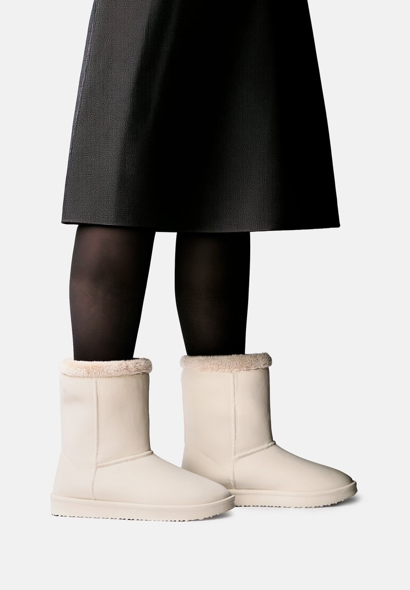 Jambes portant des collants noirs et une jupe noire associées à des bottines crème doublées d'une légère bordure en fourrure.